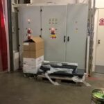 Obrázek ukazuje rozvaděče elektrické energie na pracovišti, které jsou však zabarikádované nějakým balícím materiálem jako jsou krabice, fólie a palety.
